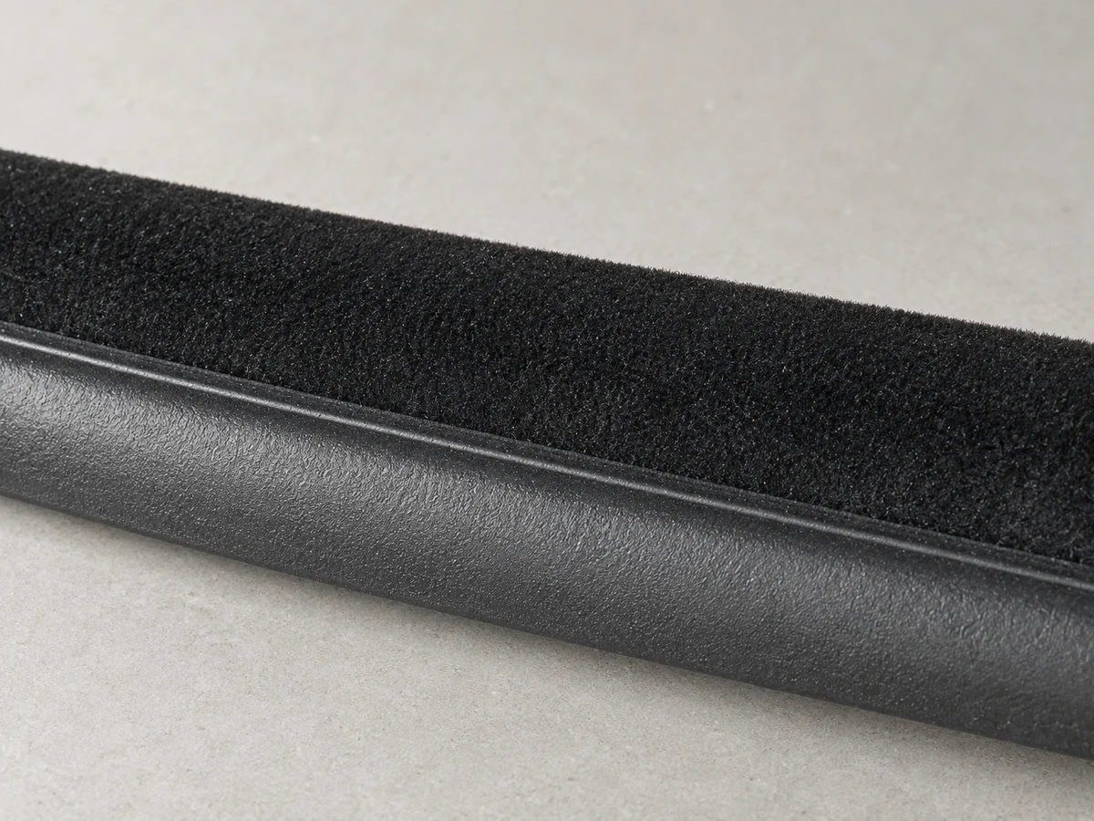 Close-up of a black flocked weatherstrip showing the short-fiber contact band and rubber base