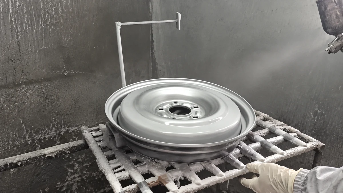 A wheel-shaped metal workpiece on a grid support in a spray booth